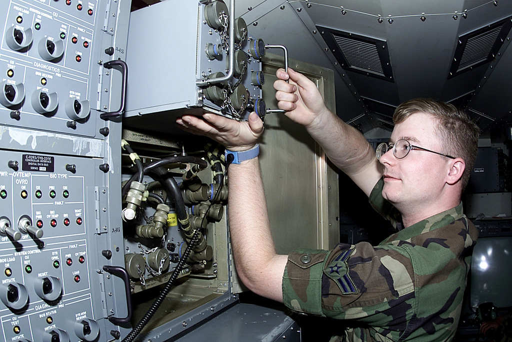 An airman works inside an open cabinet of electronic switching equipment.