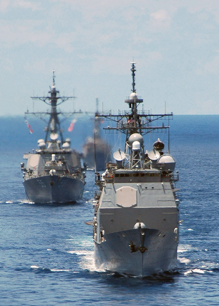 U.S. Navy ships underway in open water, seen from ahead.
